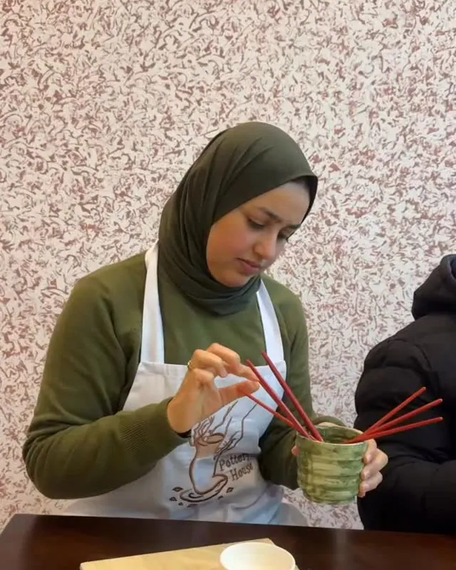 Une participante peint sa tasse devant le papier peint fleuri