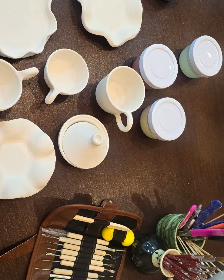 Tasses et assiettes en biscuit blanc à côté des pots de peinture